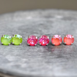 May include: Six small round earrings with silver posts. Two are green, two are pink, and two are orange.