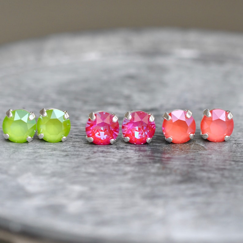May include: Six small round earrings with silver posts. Two are green, two are pink, and two are orange.