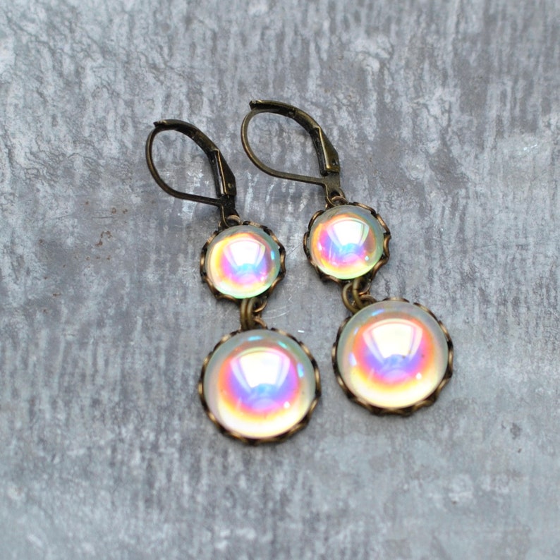 May include: A pair of iridescent glass dangle earrings with bronze-colored metal settings. The earrings feature two round glass beads on each earring.