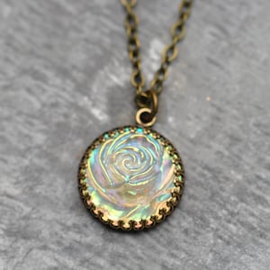 Könnte beinhalten: Eine Halskette aus Bronze mit einem runden Anhänger, der ein schimmerndes Rosenmotiv zeigt.