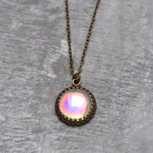 May include: A vintage-style necklace with a round pendant. The pendant features an iridescent, multi-colored stone set in a bronze-toned, filigree frame. The chain is also bronze-toned and hangs against a gray background.