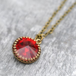 May include: A red gemstone pendant necklace with a bronze chain. The pendant is round and has a detailed, ornate design around the edge.