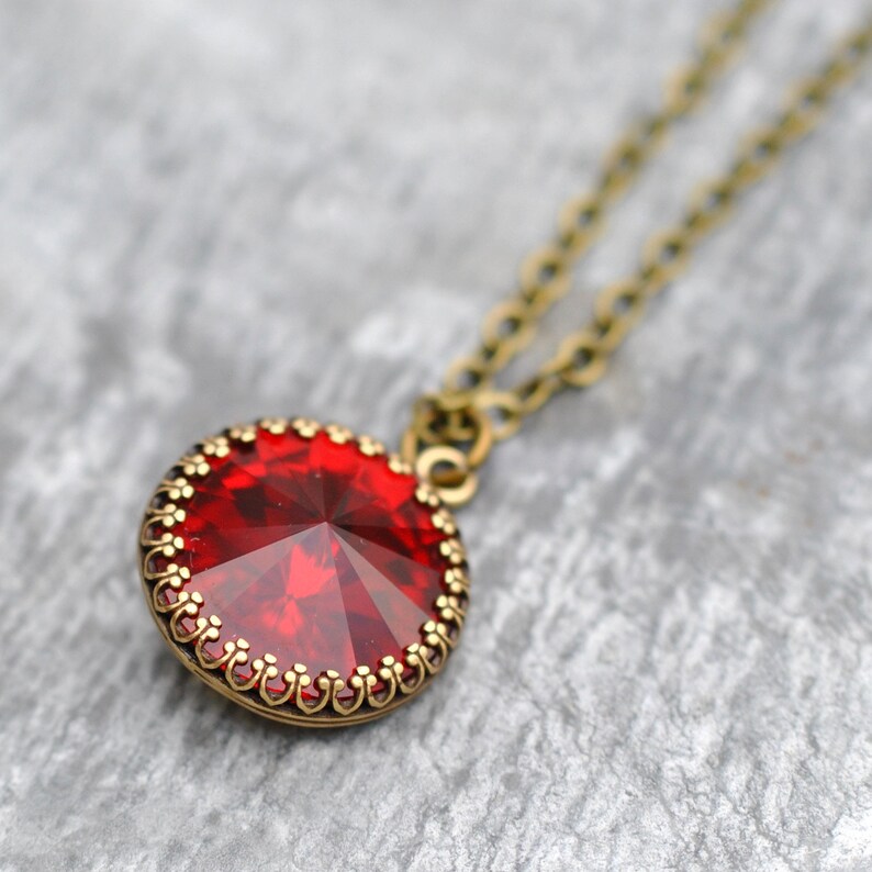 May include: A red gemstone pendant necklace with a bronze chain. The pendant is round and has a detailed, ornate design around the edge.