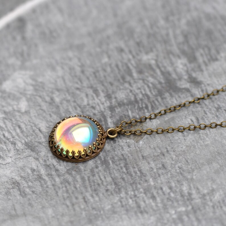 May include: A round pendant necklace with an iridescent, multi-colored stone set in a bronze-colored, ornate bezel. The necklace chain is also bronze-colored. The pendant is approximately 1 inch in diameter.
