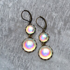 May include: A pair of iridescent glass dangle earrings with bronze-colored metal accents. The earrings feature three round glass beads, each with a different iridescent color.