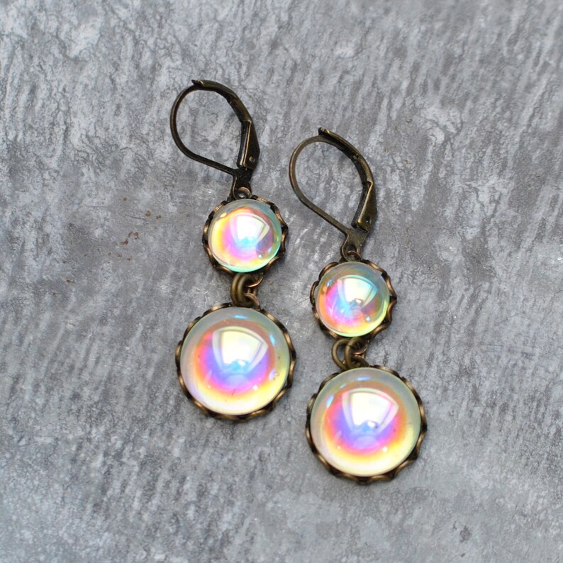 May include: A pair of iridescent glass dangle earrings with bronze-colored metal accents. The earrings feature three round glass beads, each with a different iridescent color.