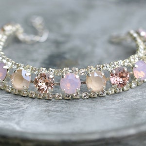 Puede incluir: Un brazalete plateado con una fila de piedras redondas de color rosa y rosa claro engastadas en un marco plateado.