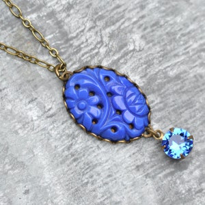 K&ouml;nnte beinhalten: Eine blaue Blumen-Halskette mit einem blauen Kristall-Anh&auml;nger. Der Anh&auml;nger ist aus geschnitztem Glas und hat eine Messingkette.