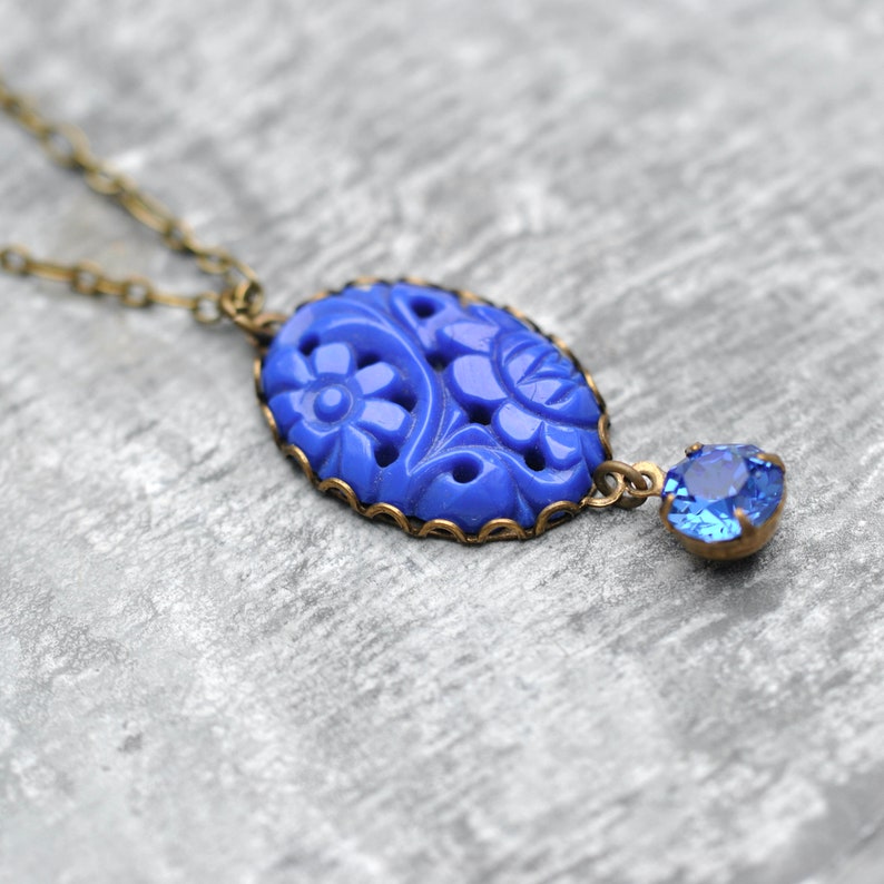 K&ouml;nnte beinhalten: Eine blaue Glaskette mit einem floralen Anh&auml;nger und einem kleineren blauen Kristall-Akzent. Die Kette hat eine Messingkette.