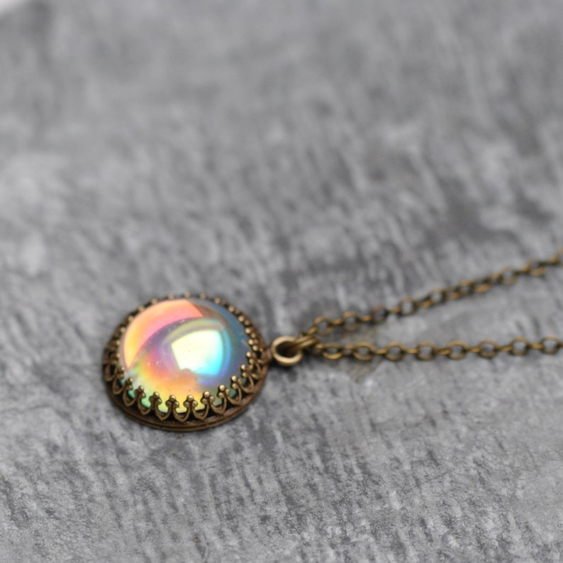 May include: A vintage-style necklace featuring a round, iridescent pendant with a bronze-colored filigree setting. The pendant reflects a spectrum of colors, including pink, yellow, and blue. The chain is also bronze-colored.