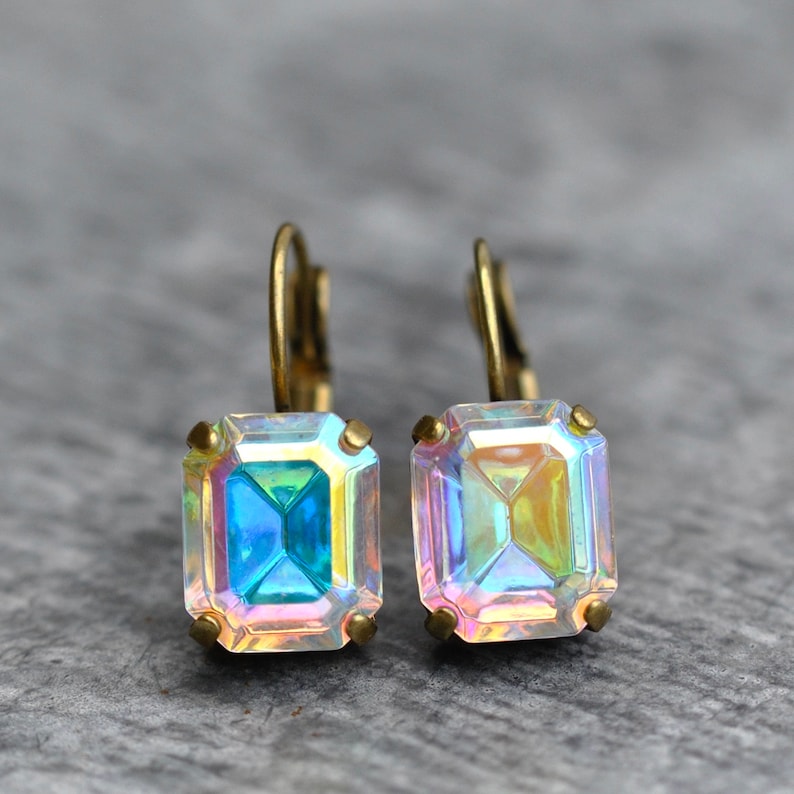 May include: A pair of iridescent gold earrings with square-shaped gemstones. The gemstones have a rainbow effect.