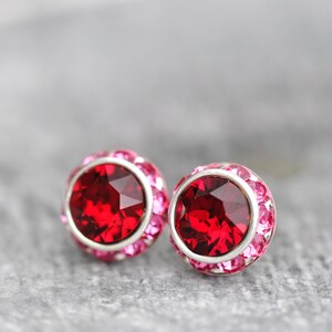 May include: A pair of silver stud earrings with a red crystal centre surrounded by a halo of pink crystals.