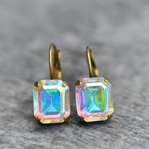 May include: A pair of gold earrings with iridescent square-shaped gemstones. The earrings have a simple, elegant design.