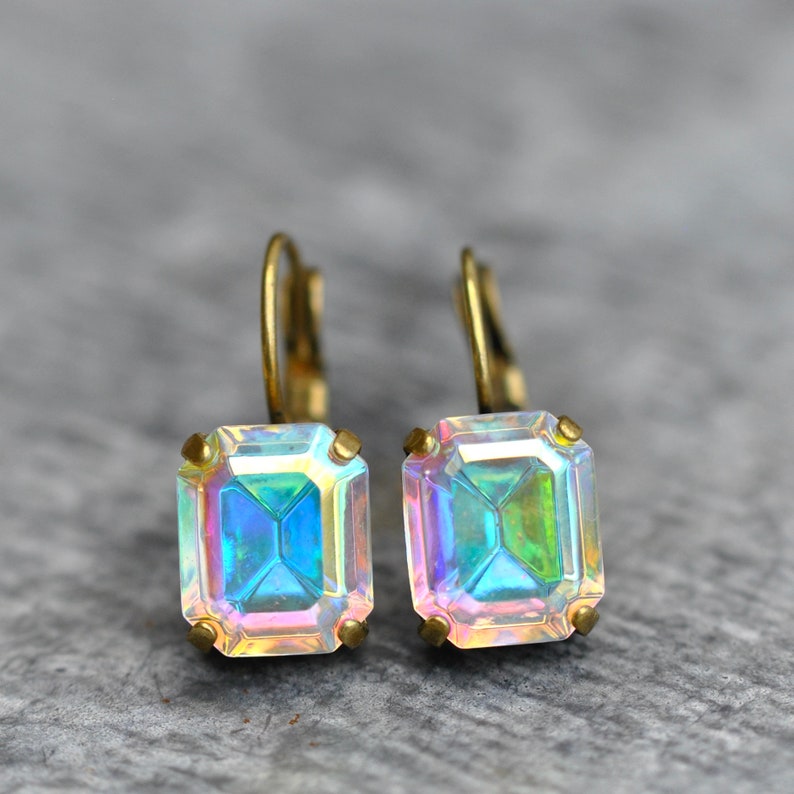 May include: A pair of gold earrings with iridescent square-shaped gemstones. The earrings have a simple, elegant design.