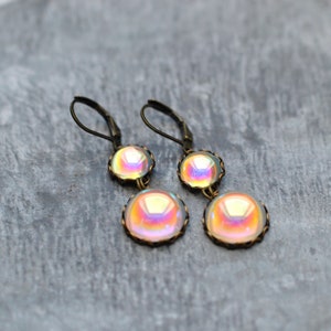 May include: A pair of iridescent glass dangle earrings with bronze-colored metal settings. The earrings have two round glass beads on each earring.