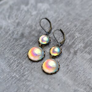 May include: A pair of iridescent glass dangle earrings with antique bronze settings. The earrings feature two round glass beads on each earring, with a smaller bead above a larger bead.