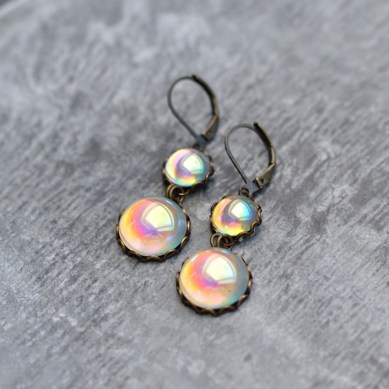 May include: A pair of iridescent glass dangle earrings with antique bronze settings. The earrings feature two round glass beads on each earring, with a smaller bead above a larger bead.