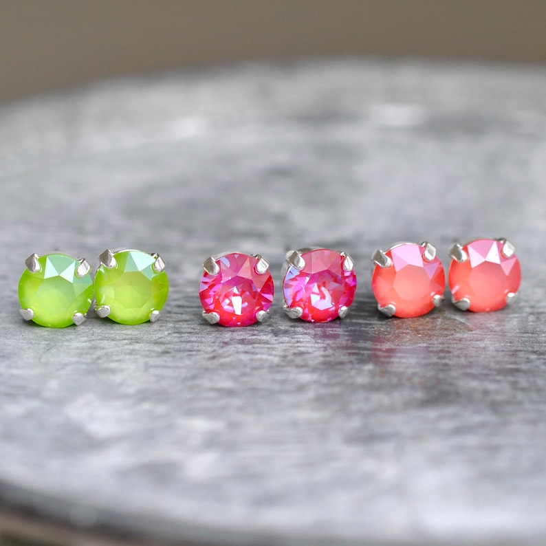 May include: Three pairs of earrings with silver posts and colorful crystal stones. The first pair has green stones, the second pair has pink stones, and the third pair has orange stones.