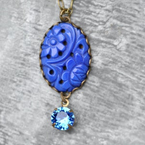 K&ouml;nnte beinhalten: Eine blaue und goldene Halskette mit einem Anh&auml;nger mit geschnitztem Blumenmuster und einem blauen Kristalltropfen.