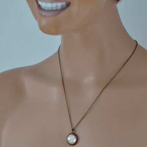 May include: A bronze-toned necklace with a round pendant. The pendant has a shimmering, iridescent center and a decorative border. The necklace is displayed on a mannequin.