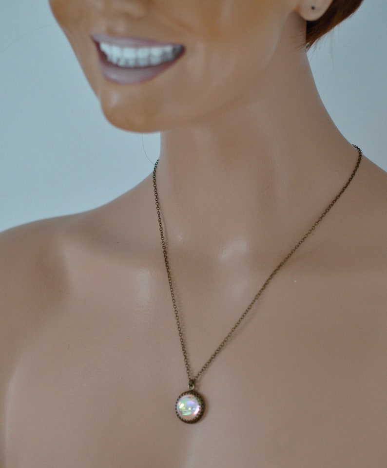 May include: A bronze-toned necklace with a round pendant. The pendant has a shimmering, iridescent center and a decorative border. The necklace is displayed on a mannequin.