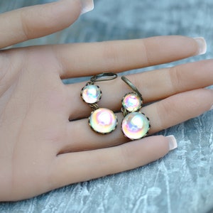 May include: A pair of iridescent glass dangle earrings with bronze-colored metal settings. The earrings feature three round glass beads, each with a different iridescent color.