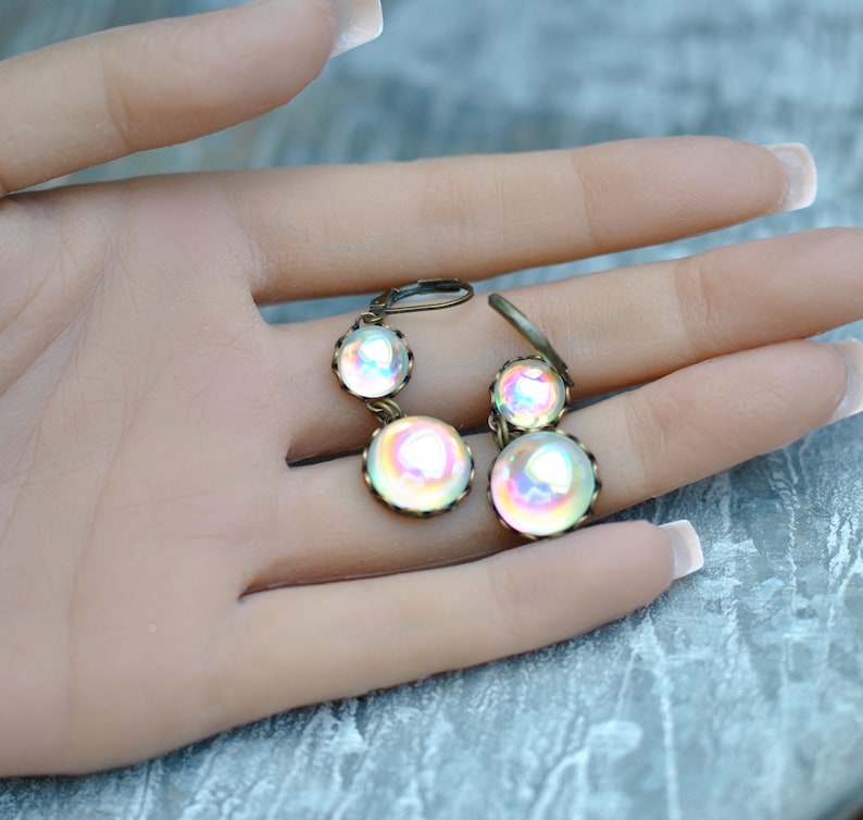 May include: A pair of iridescent glass dangle earrings with bronze-colored metal settings. The earrings feature three round glass beads, each with a different iridescent color.