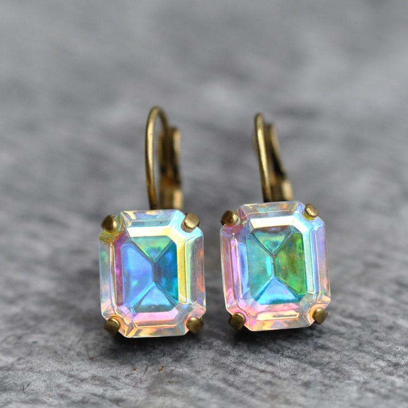 May include: A pair of iridescent gold earrings with square-shaped gemstones. The gemstones have a rainbow-like effect.