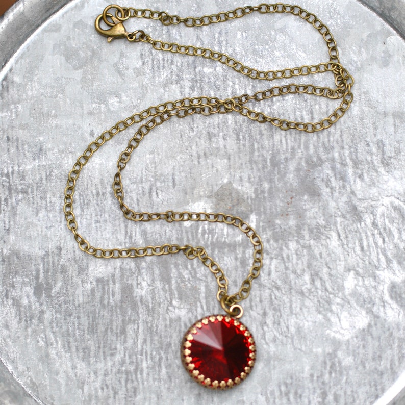 May include: A red gemstone pendant necklace with a gold chain. The pendant is round and has a faceted design.