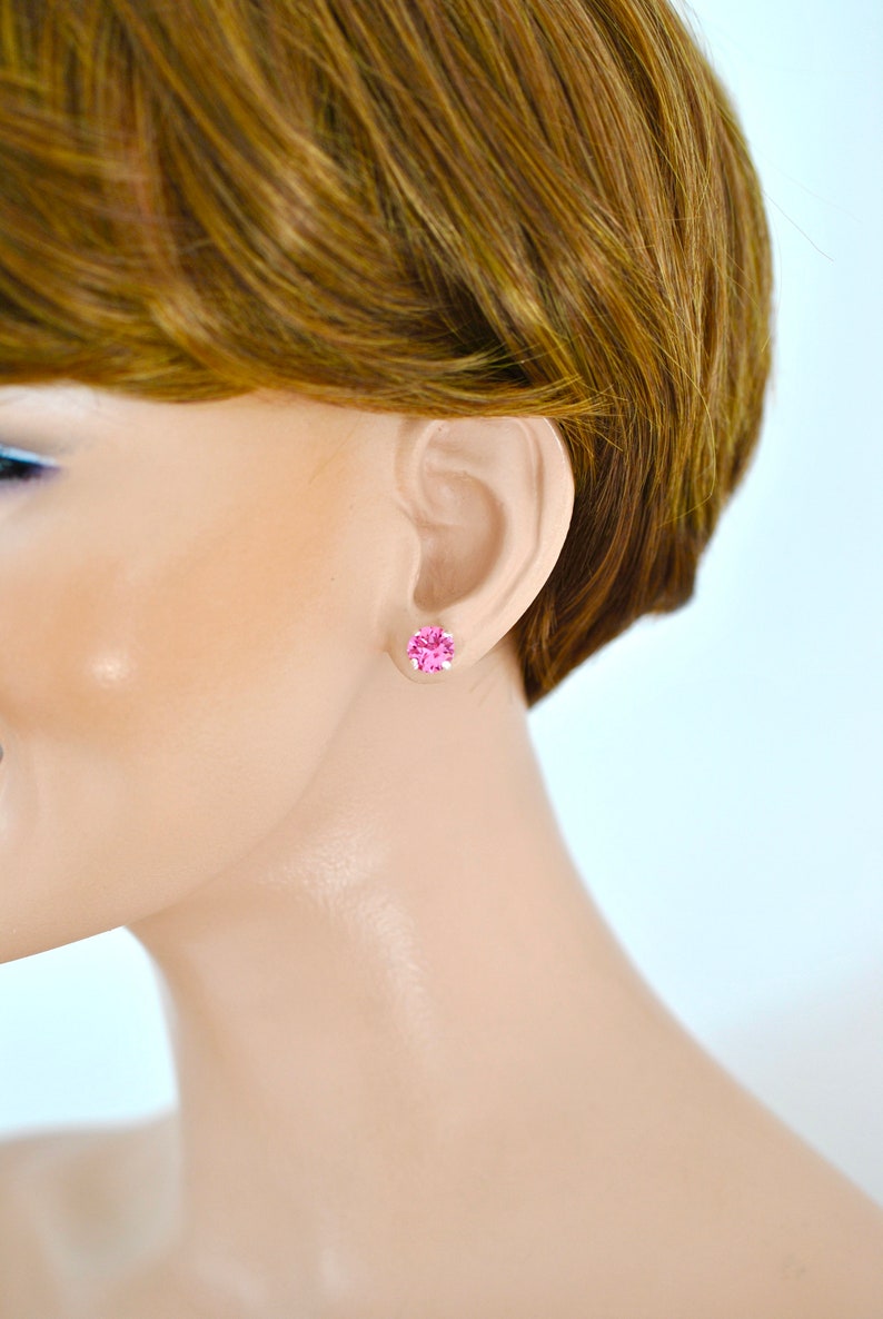 May include: A pair of small pink stud earrings with a round, faceted stone.