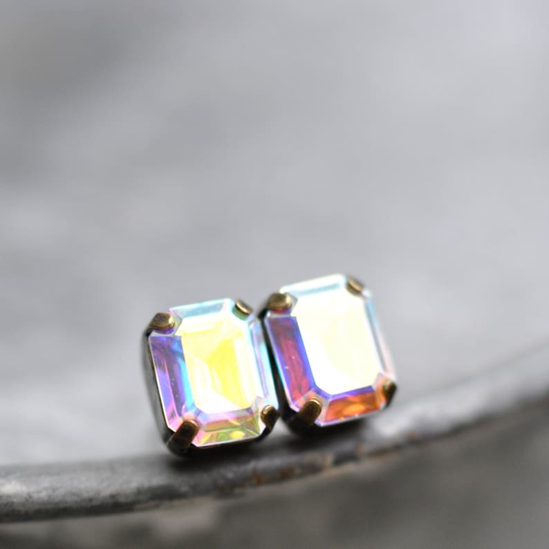 Puede incluir: Un par de pendientes de color iridiscente con forma de esmeralda y engastes dorados. Los pendientes son peque&ntilde;os y delicados.