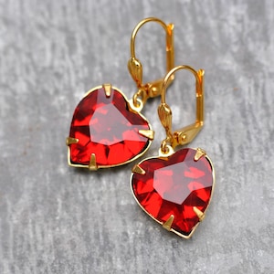 Puede incluir: Un par de pendientes de corazón de oro con detalles de cristal rojo.