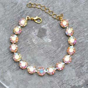 May include: A gold-toned bracelet featuring iridescent, round crystals. The crystals are set in a delicate gold chain, with a lobster clasp closure and an adjustable chain. The crystals reflect a rainbow of colors.