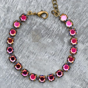May include: A pink iridescent crystal bracelet with a brass clasp. The bracelet is made of small, round crystals that are set in a brass setting.