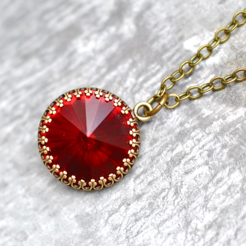 May include: A red crystal pendant necklace with a gold-toned chain and a decorative filigree border around the crystal.
