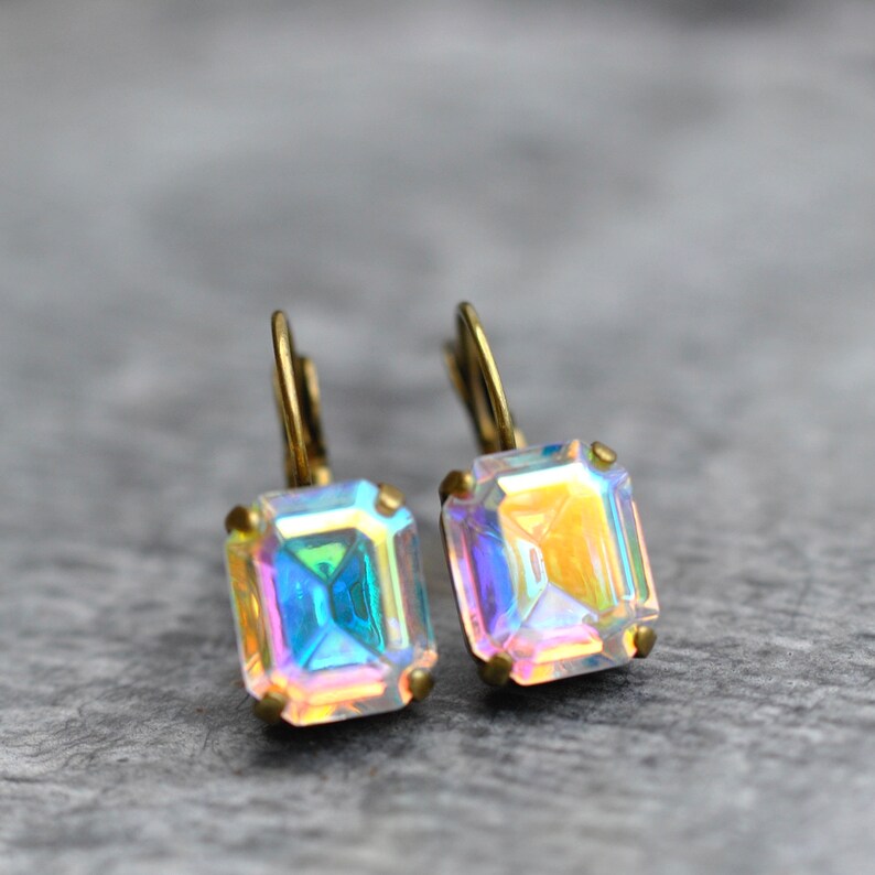 May include: A pair of iridescent gold earrings with square-shaped crystals. The crystals have a rainbow effect.