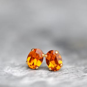 Könnte beinhalten: Ein Paar goldene Ohrstecker mit orangefarbenen Edelsteineinsätzen.