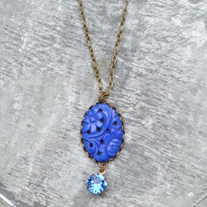 K&ouml;nnte beinhalten: Eine blaue Blumen-Halskette mit einem kleinen blauen Kristall-Anh&auml;nger. Die Halskette ist aus Messing und hat eine zarte Kette.