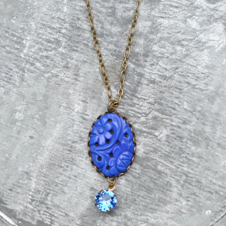 K&ouml;nnte beinhalten: Eine blaue Blumen-Halskette mit einem kleinen blauen Kristall-Anh&auml;nger. Die Halskette ist aus Messing und hat eine zarte Kette.