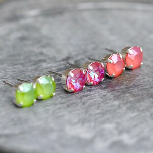 May include: A set of six earrings with silver posts and colorful crystal stones. The earrings are arranged in a row, with two green, two pink, and two coral stones.