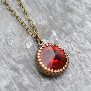 May include: A red gemstone pendant necklace with a brass chain. The pendant is round and has a gold-coloured bezel with a decorative edge.