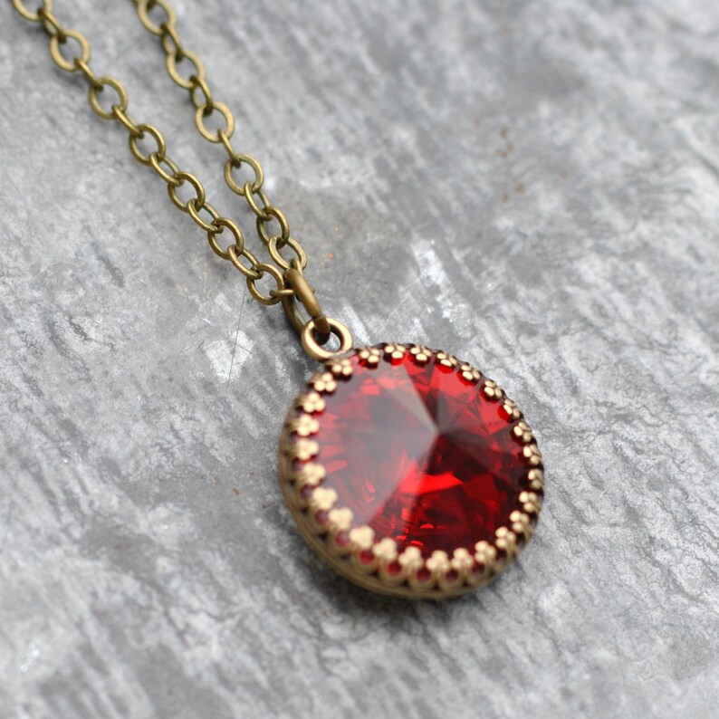 May include: A red gemstone pendant necklace with a brass chain. The pendant is round and has a gold-coloured bezel with a decorative edge.
