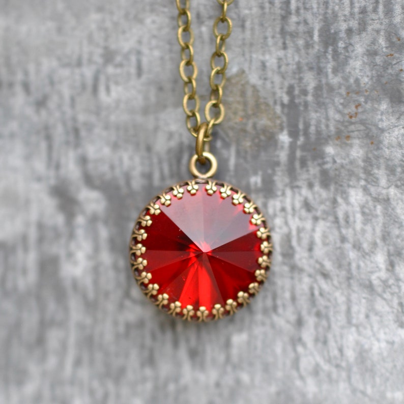 May include: A red crystal pendant necklace with a gold-toned chain and a decorative border around the crystal.