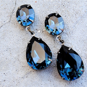 Puede incluir: Un par de pendientes colgantes con dos cristales azules en forma de lágrima en cada pendiente. Los cristales son facetados y tienen un color azul oscuro.