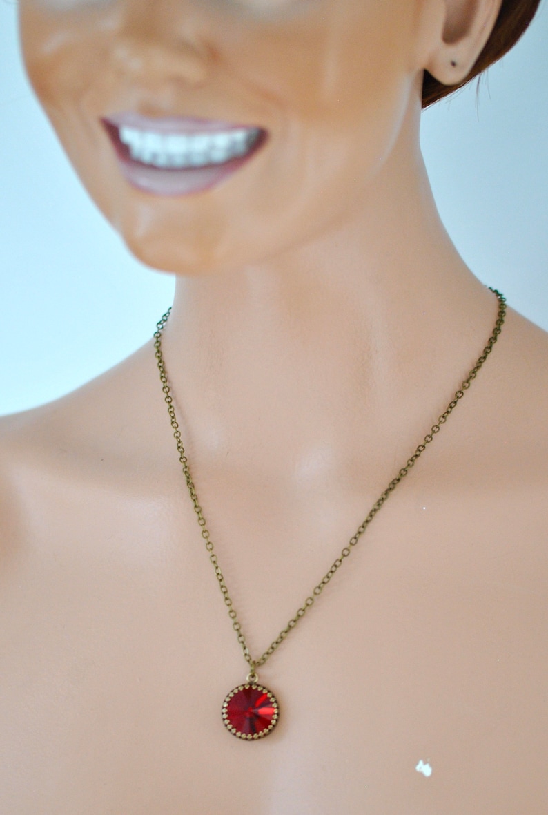 May include: A red gemstone pendant necklace with a bronze chain. The pendant is round and has a faceted design.