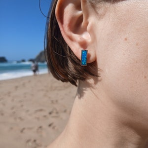 Może przedstawiać: Para srebrnych kolczyków z prostokątnym niebieskim opalem.