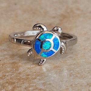 May include: A silver ring with a blue opal turtle design. The turtle's shell is decorated with a blue opal stone.