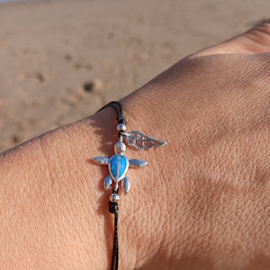 May include: A black string bracelet with a silver turtle charm with a blue opal inlay and a silver wing charm.