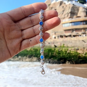 Puede incluir: Una pulsera de cadena plateada con eslabones circulares alternos con diseño de espiral y piedras redondas de color azul vibrante similares al ópalo. La pulsera incluye un cierre de mosquetón y está formada por segmentos de metal pulido.