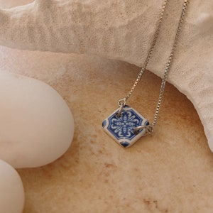 Può includere: Una collana con catena d'argento con un ciondolo in ceramica blu e bianca con un motivo floreale.